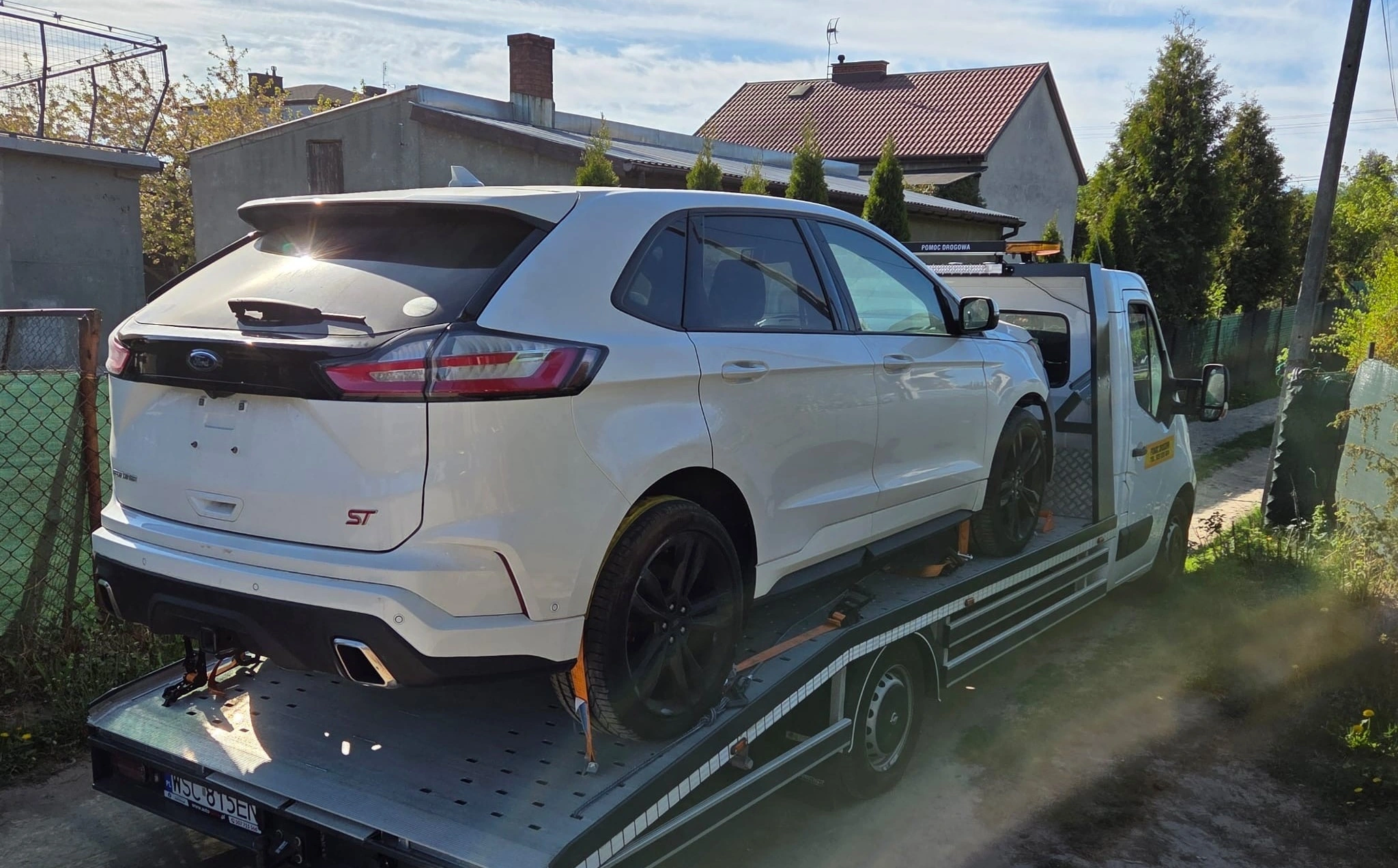 Biały Ford Edge ST zabezpieczony pasami na platformie lawety
